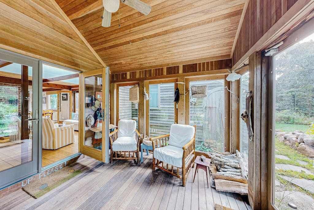 A wooden deck with wicker chairs, a glass door leading to a room, and a view of the outdoors.