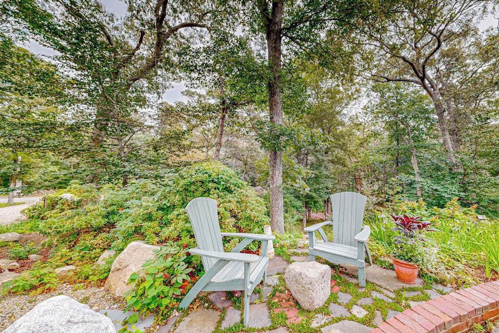 Duas cadeiras Adirondack em um jardim com caminhos de pedra e vegetação exuberante.