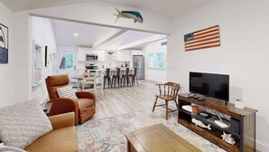 Un soggiorno moderno con divano, TV e mobile TV in legno. In secondo piano si nota un'area pranzo con sedie e tavolo.