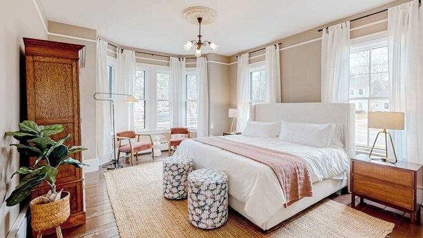 Ein Schlafzimmer mit einem großen Bett, zwei Hocker, einem Holzschrank, einem Schreibtisch und einem Sessel.