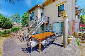 A two-story house with a wooden deck, a staircase, and a dining area with a table and chairs.
