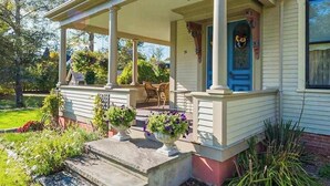 Ein Haus mit einer Veranda, einer blauen Tür und einem Garten mit Blumentöpfen.