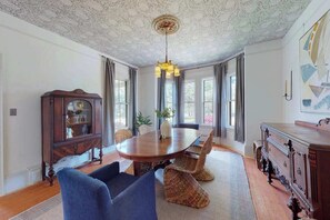 A dining room with a wooden table, wicker chairs, a chandelier, and a large window with curtains.