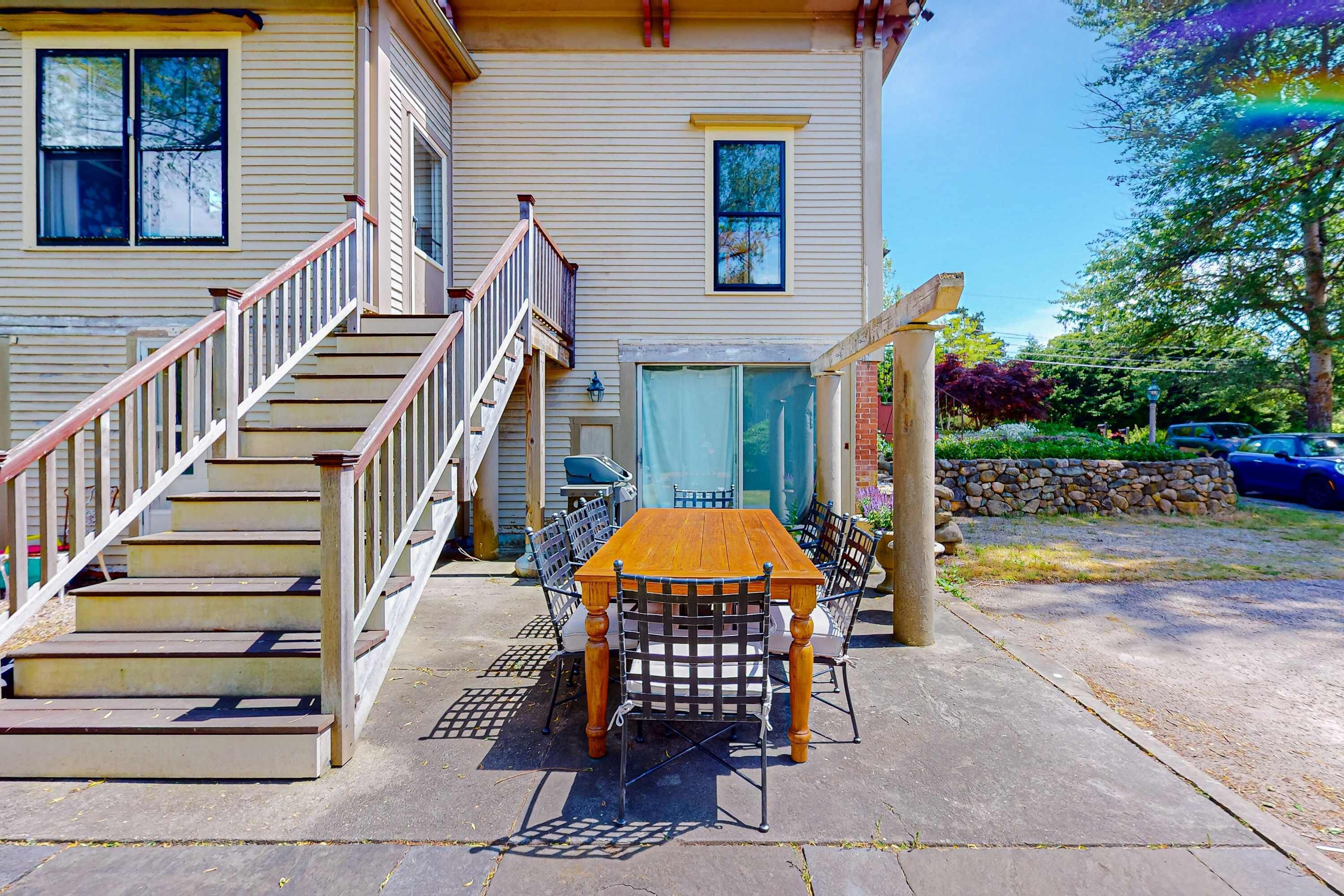 Ein zweistöckiges Haus mit einer Holztreppe, einer Terrasse mit Tisch und Stühlen sowie einem überdachten Bereich mit Tisch und Stühlen.