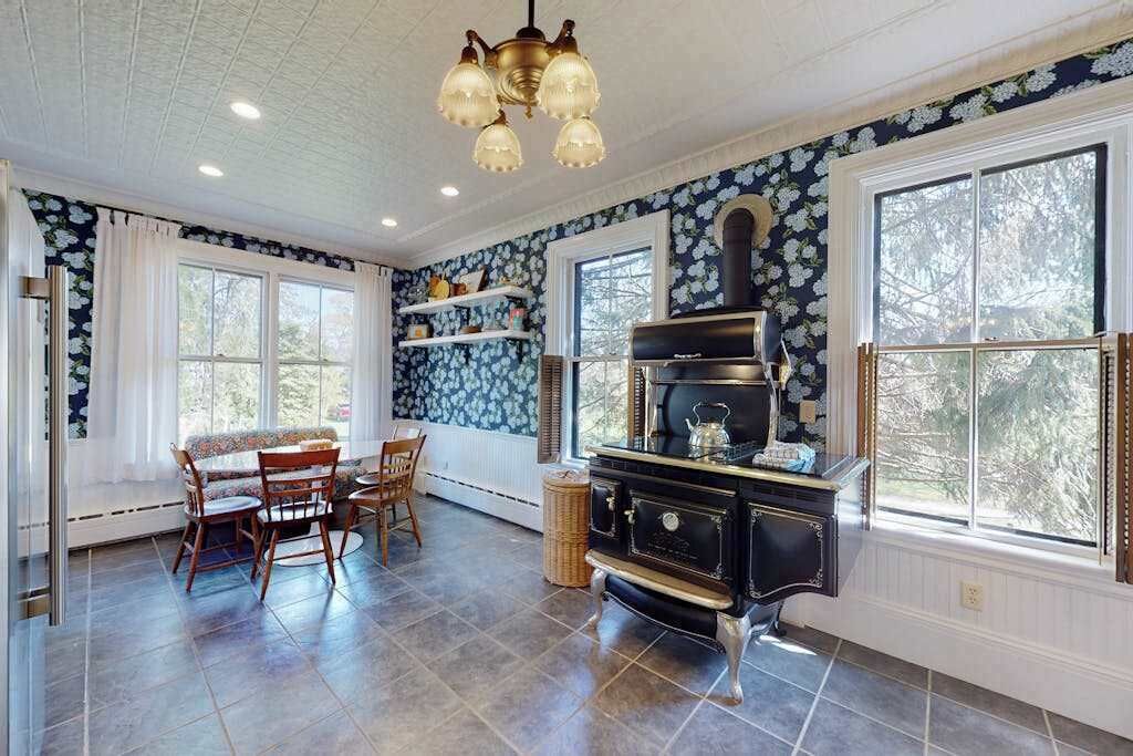 A kitchen with a black stove, wooden chairs, and a window with a view of trees.