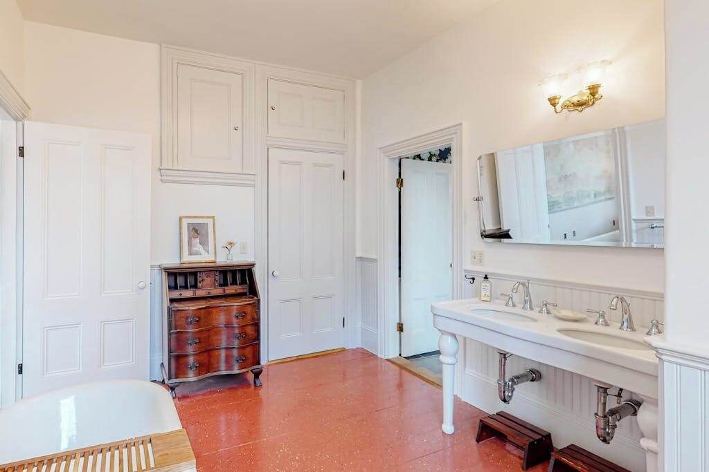 A bathroom with a white bathtub, a vanity with a mirror, and a wooden dresser.