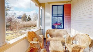 Eine Veranda mit Korbmöbeln, ein Fenster mit Rollläden und Blick ins Freie.