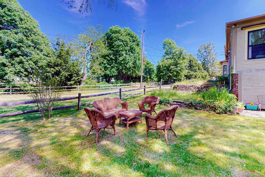 Une cour arrière clôturée, aménagée avec du mobilier d’extérieur, une terrasse en bois et une maison.
