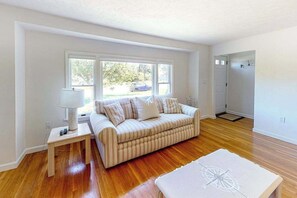 Ein Zimmer mit einer gestreiften Couch, einem kleinen Tisch mit einer Lampe und einem großen Fenster mit Blick auf ein Auto und Grünfläche.