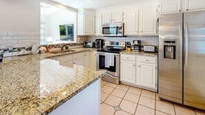 Een moderne keuken met witte kasten, granieten aanrechtbladen, roestvrijstalen apparatuur en een groot raam.
