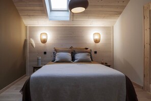 Ein Schlafzimmer mit einem Bett, zwei Wandlampen, einem Oberlicht und einer Holzbalkendecke.