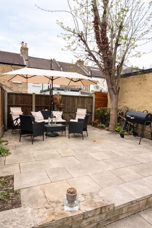 Eine Terrasse mit Gartenmöbeln, einem Grill und einem Baum.