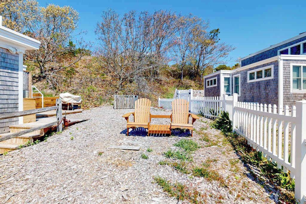 Une terrasse en bois avec des fauteuils Adirondack, une clôture blanche en bois et un bâtiment à la façade en pierre.
