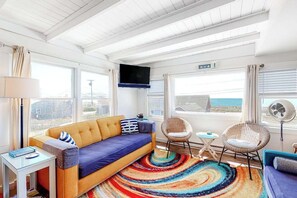 Ein modernes Zimmer mit einer Couch, Sesseln, einem Fernseher und Meerblick.