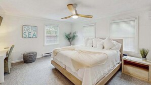 Une chambre à coucher avec un lit, un ventilateur de plafond, un panneau fixé au mur et une fenêtre avec des stores.