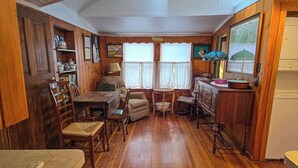 A wooden interior with a dining table, chairs, a small round table, a cabinet, and a television.