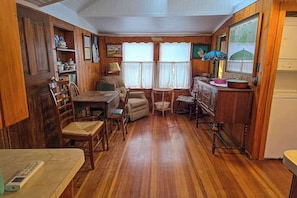 A wooden interior with a dining table, chairs, a small round table, a cabinet, and a television.