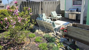 A backyard with a wooden deck, a grill, outdoor furniture, and flowering plants.