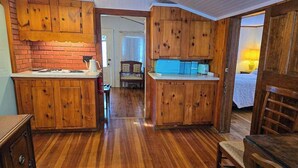 A kitchen with wooden cabinets and a brick backsplash, a dining area with a wooden table and chairs, and a visible door leading to another room.