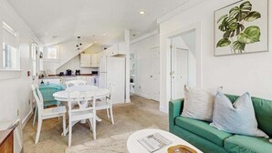 A modern kitchen with white cabinets, a dining area with a white table and chairs, and a green sofa in the living room. - Heart of Provincetown Penthouse - perfect location...walk to everything! (Provincetown)