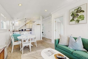 A modern kitchen with white cabinets, a dining area with a white table and chairs, and a green sofa in the living room.