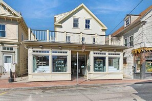 A two-story building with a balcony, storefronts on the ground floor, and a clear sky.