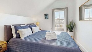 A bedroom with a bed, pillows, a bedside lamp, a window, and a plant. - Heart of Provincetown Penthouse - perfect location...walk to everything! (Provincetown)