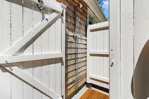 Une porte en bois peinte en blanc, dotée d’une poignée en métal, une terrasse en bois et un tuyau en métal qui longe le mur.