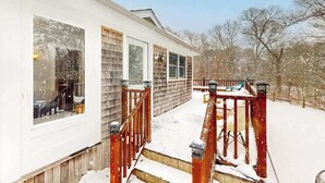 Una casa con terraza de madera, un porche cubierto y un patio cubierto de nieve.