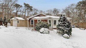 Una casa cubierta de nieve con porche delantero, garaje y árboles nevados.