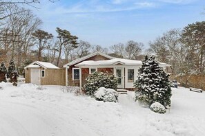 Ein mit Schnee bedecktes Haus mit Veranda, Garage und schneebedeckten Bäumen.