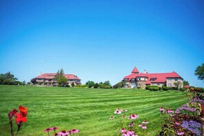 A large, multi-story building with a red roof, surrounded by a well-maintained lawn and various flowers. - Relaxing fairway escape with resort pools, club access, & steps to Arbor Pool (Brewster)