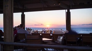 Een restaurant aan zee met terras, uitzicht op de oceaan en flessen op de bar.