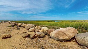 A beach with large rocks, a grassy area, and a clear blue sky.