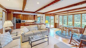 A spacious living area with a sofa, coffee table, and dining table. A kitchen with wooden cabinets and appliances is visible in the background.