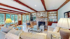 A spacious living room with a fireplace, wooden beams, and a large window.