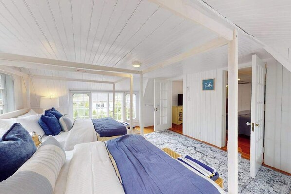 A room with two beds, a wooden ceiling, a view through a door, and a sign on the wall.