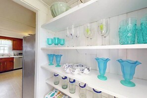A kitchen with white cabinets, a stainless steel refrigerator, and shelves with glassware.