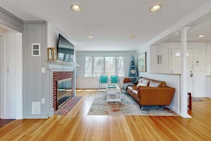 A living room with a fireplace, a sofa, a coffee table, and a TV. - Spacious coastal retreat close to beach with modern kitchen, deck, AC, & sunroom (Yarmouth)