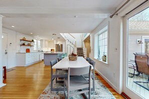 A spacious kitchen with white cabinets, a central island, and a dining area with a large table and chairs. - Spacious coastal retreat close to beach with modern kitchen, deck, AC, & sunroom (Yarmouth)