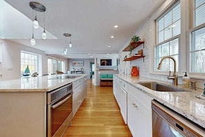 A modern kitchen with a central island, built-in appliances, and a large window providing natural light. - Spacious coastal retreat close to beach with modern kitchen, deck, AC, & sunroom (Yarmouth)