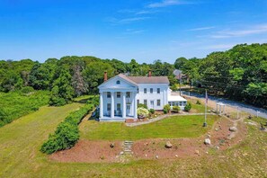 A large white house with a central portico, surrounded by lush greenery and a river. - Grand home with historic charm, game room & spacious outdoor living spaces (South Dennis)