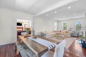 A spacious living room with a wooden dining table, a sofa set, and a fireplace. - Grand home with historic charm, game room & spacious outdoor living spaces (South Dennis)