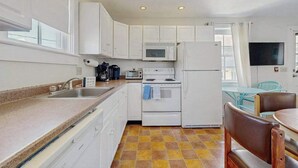 Una cocina compacta con gabinetes blancos, microondas, estufa, refrigerador, lavaplatos y un comedor con mesa y sillas.