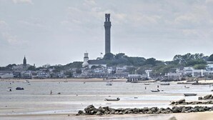Un pueblo costero con un faro destacado, una playa de arena y barcos.