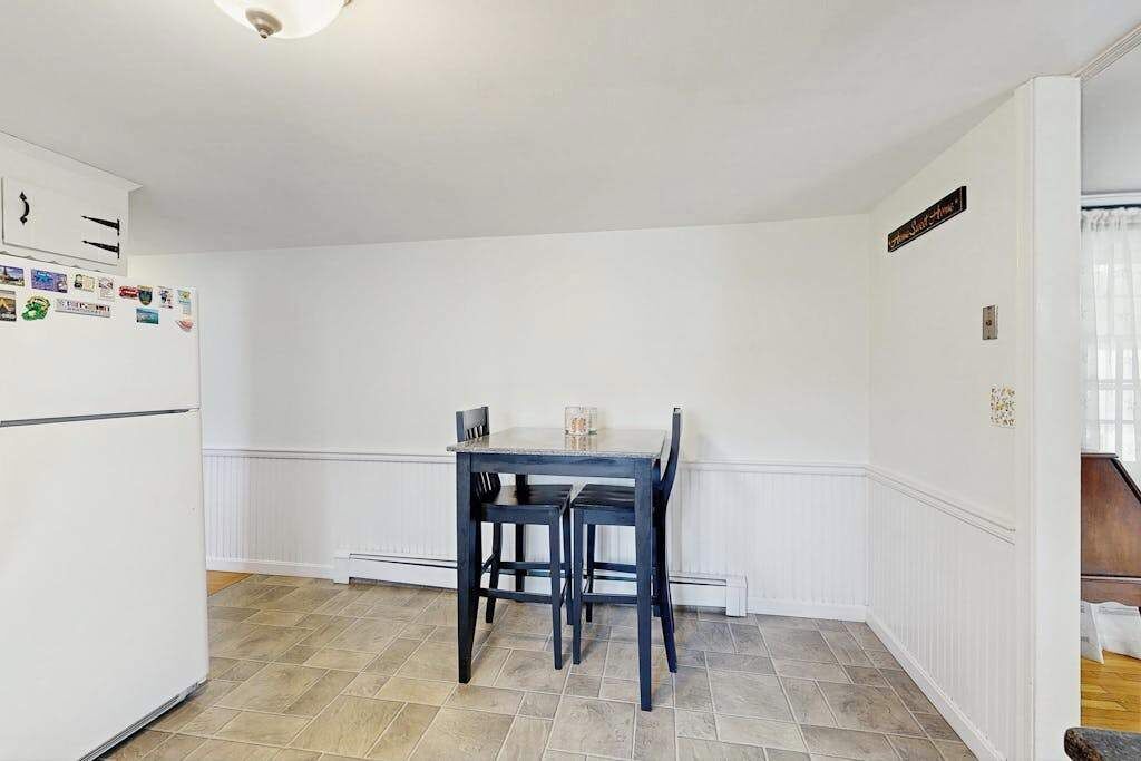 A kitchen with a white refrigerator, a dining table with chairs, and a white wall with a sign.