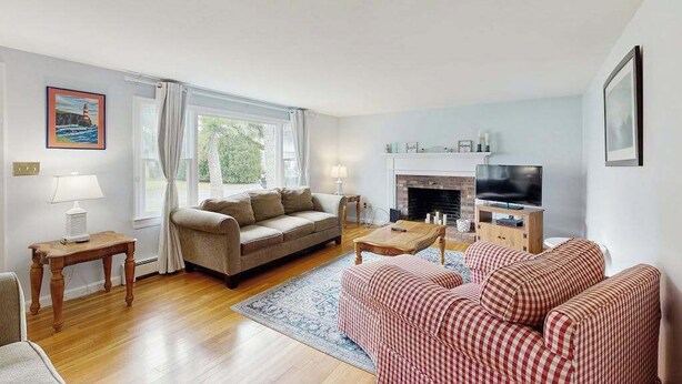 Ein Wohnzimmer mit einer Couch, einem rot-weißen Karomuster-Sofa, einem Fernseher, einem Kamin und einem Fenster mit Vorhängen.