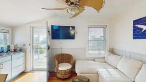 Ein Zimmer mit Deckenventilator, einem weißen Sofa, einem Korbstuhl, einem Fernseher und einem Fenster mit Jalousien.