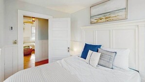 Ein Schlafzimmer mit Bett, einem Gemälde, einer Tür und einem Flur.