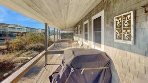 Eine überdachte Veranda mit Grill, Bank und einem Schild mit der Aufschrift 'BEACH HOUSE'.